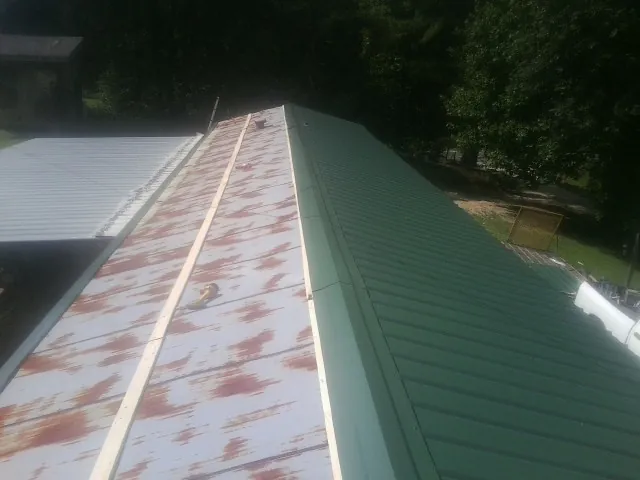 Old rusted panels beside newly installed green metal roofing — Wind Damage Roof Repair by Roofing Brothers in West Memphis