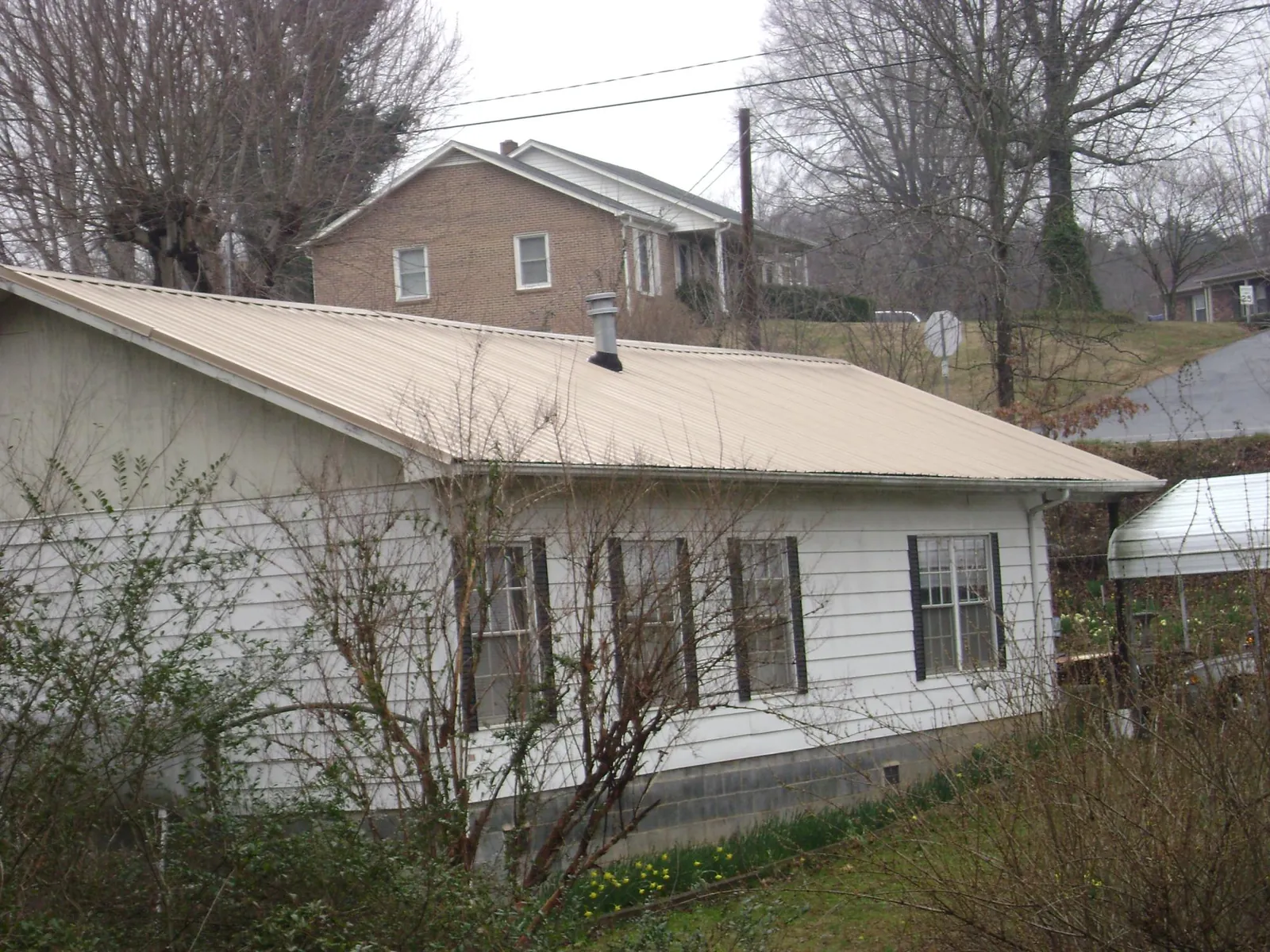 Tan metal roof on a white sided house set into a hillside — Commercial Roofing by Roofing Brothers in West Memphis
